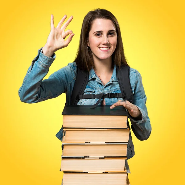 Adolescente estudiante chica con un montón de libros y haciendo OK signo — Foto de Stock