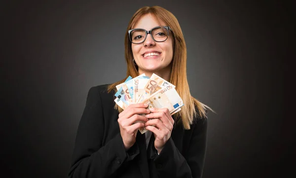 Joven mujer de negocios tomando un montón de dinero en el fondo oscuro — Foto de Stock