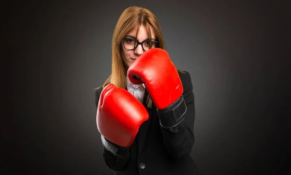 Jovem mulher de negócios com luvas de boxe no fundo escuro — Fotografia de Stock