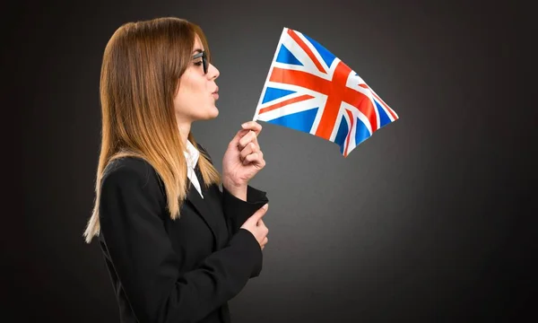 Joven mujer de negocios sosteniendo una bandera del Reino Unido sobre fondo oscuro — Foto de Stock