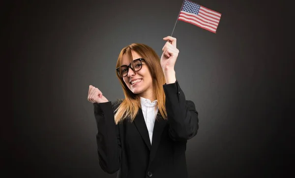 Joven mujer de negocios sosteniendo una bandera americana sobre fondo oscuro —  Fotos de Stock