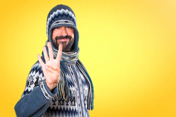 Чоловік з зимовим одягом, що рахує чотири на барвистому фоні — стокове фото