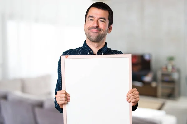Hombre guapo sosteniendo un cartel vacío dentro de la casa — Foto de Stock