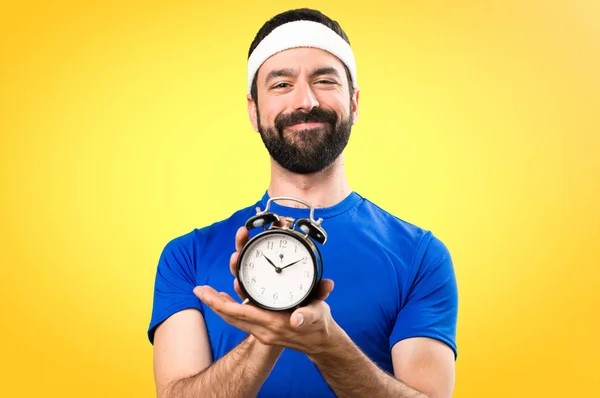 Fröhlicher lustiger Sportler mit Oldtimer-Uhr auf buntem Hintergrund — Stockfoto