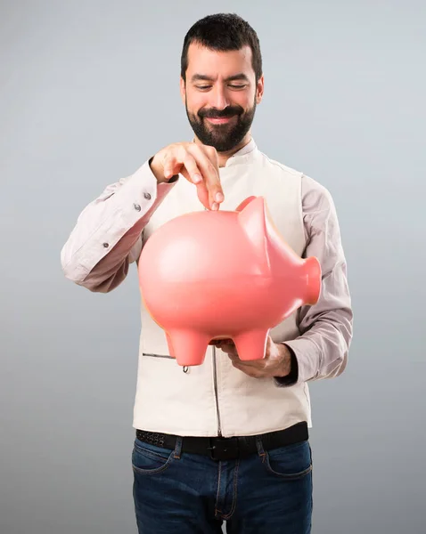 Knappe man met vest houden een spaarpot op grijze achtergrond — Stockfoto