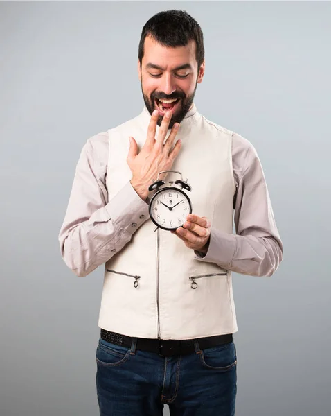 Bonito homem com colete segurando relógio no fundo cinza — Fotografia de Stock