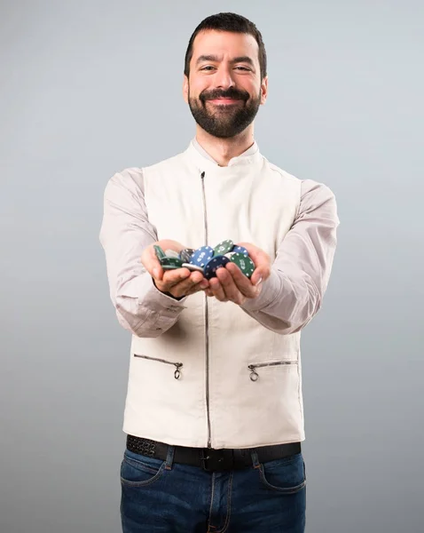 Knappe man met vest houden pokerfiches over grijze achtergrond — Stockfoto