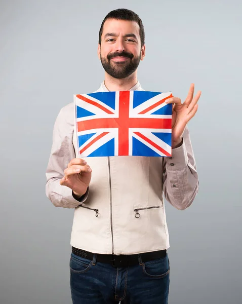 Beau homme avec gilet tenant un drapeau du Royaume-Uni sur ba gris — Photo