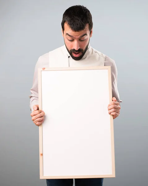 Bonito homem com colete segurando um cartaz vazio no backgrou cinza — Fotografia de Stock