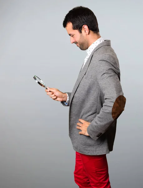 Hombre guapo con lupa sobre fondo gris — Foto de Stock