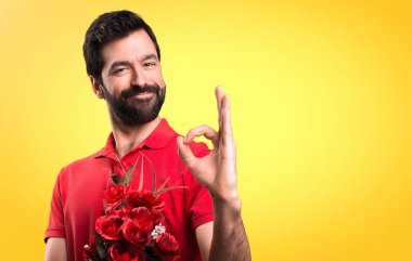 Yakışıklı adam sarı arka plan üzerinde oturum Tamam yapma çiçek tutan