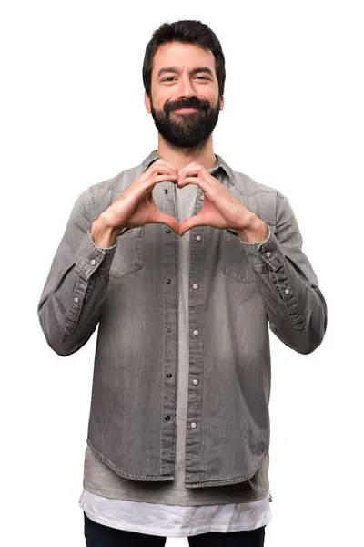 Bonito homem com barba fazendo um coração com as mãos no branco b — Fotografia de Stock