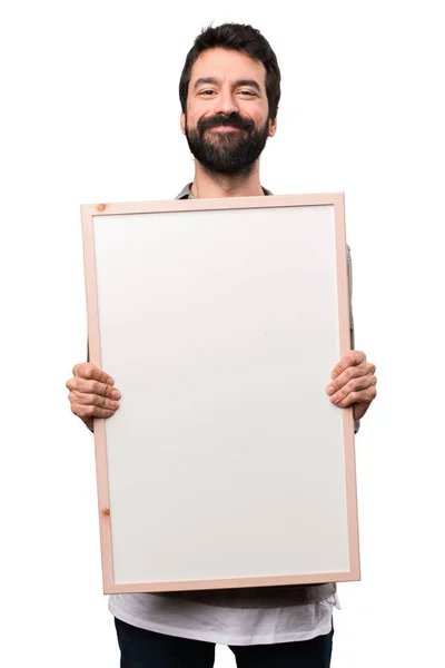 Bonito homem com barba segurando um cartaz vazio no backgr branco — Fotografia de Stock