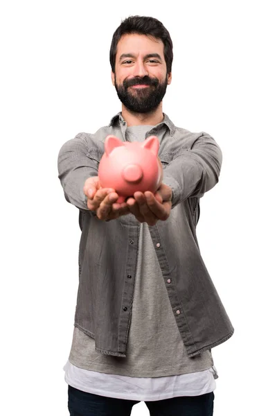 Handsome man with beard holding a piggybank on white background — Stock Photo, Image
