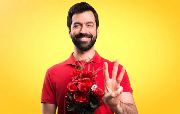 Bell'uomo che tiene i fiori contando tre su sfondo giallo — Foto Stock