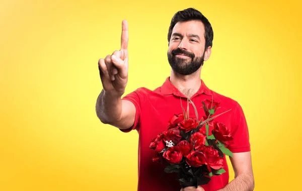 Bello uomo che tiene i fiori toccando sullo schermo trasparente su sfondo giallo — Foto Stock