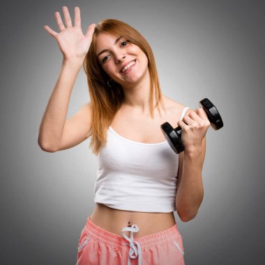 Güzel spor kadın gri arka plan üzerinde selamlayan dumbbells ile