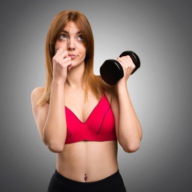 Güzel spor kadın gri arka plan üzerinde düşünme dumbbells ile