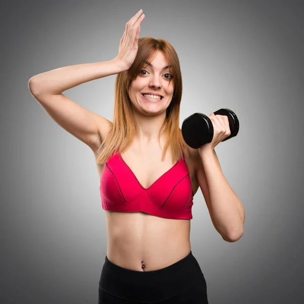 Beautiful sport woman with dumbbells having doubts on grey backg — Stock Photo, Image