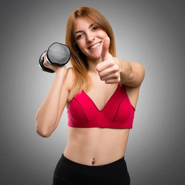 Beautiful sport woman with dumbbells with thumb up on grey backg — Stock Photo, Image