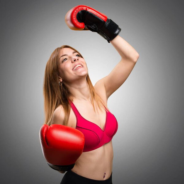 Young sport woman with boxing gloves on grey background