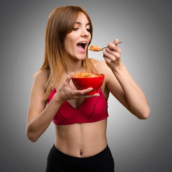 Молодая спортсменка ест злаки из миски на сером фоне — стоковое фото