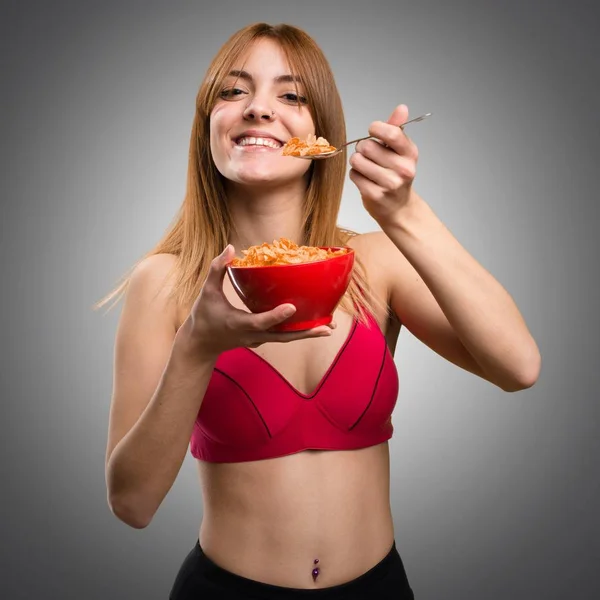 Jovem mulher esportiva comendo cereais de uma tigela em fundo cinza — Fotografia de Stock