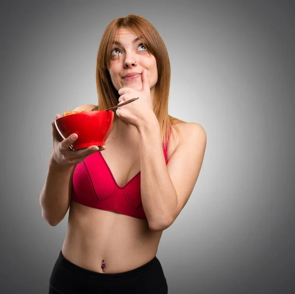Jeune femme sportive mangeant des céréales dans un bol sur fond gris — Photo
