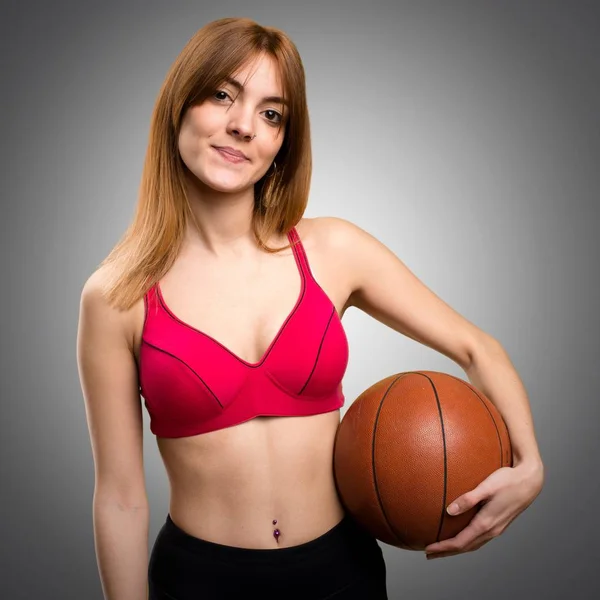 Jovem mulher do esporte com bola de basquete no fundo cinza — Fotografia de Stock