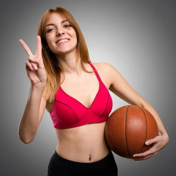 Jovem mulher do esporte com bola de basquete no fundo cinza — Fotografia de Stock