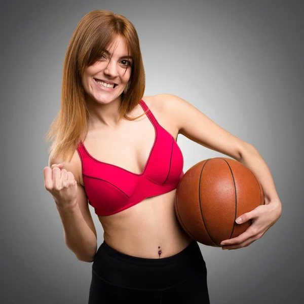 Jovem mulher do esporte com bola de basquete no fundo cinza — Fotografia de Stock