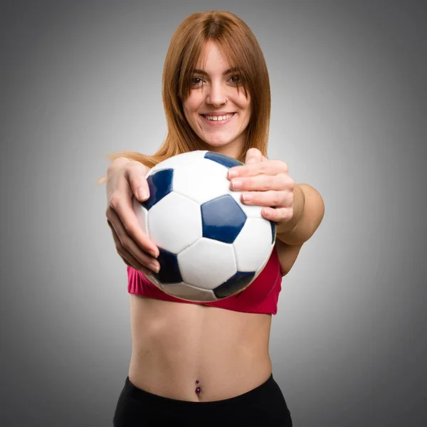 Junge Sportlerin hält einen Fußballball auf grauem Hintergrund — Stockfoto