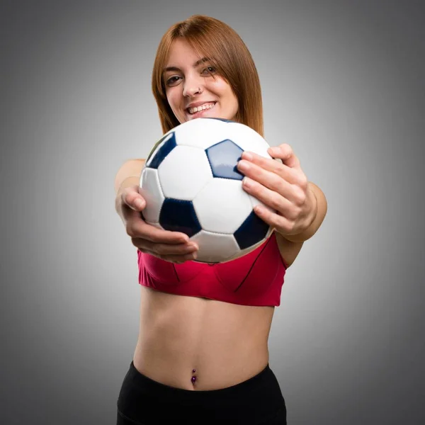 Jovem mulher esporte segurando uma bola de futebol no fundo cinza — Fotografia de Stock