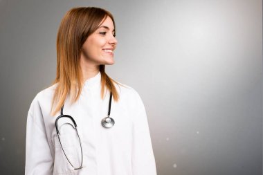 Gri arka plan üzerinde yanal arayan genç doktor kadın