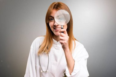 Genç doktor kadın gri arka plan üzerinde büyüteç ile