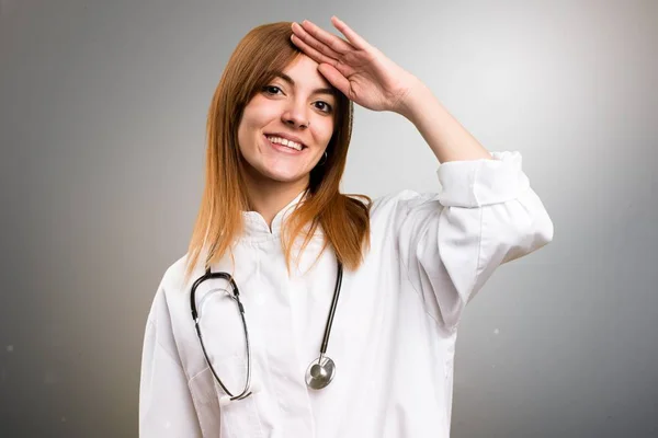 Mladý lékař žena zdravit na šedém pozadí — Stock fotografie