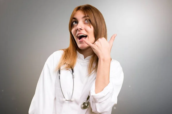 Молода лікарка робить жест телефону на сірому фоні — стокове фото