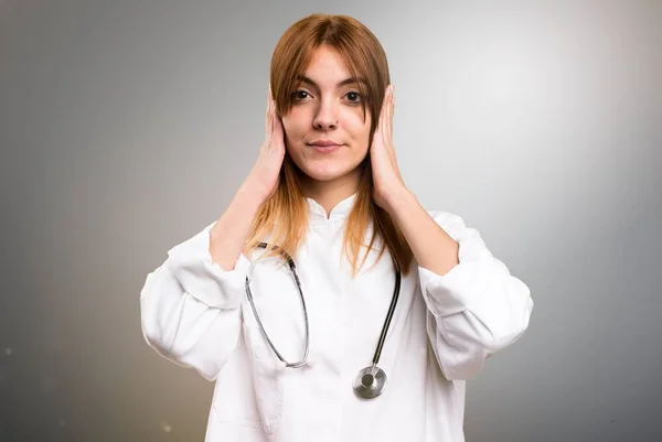 Jovem médico mulher cobrindo seus ouvidos em fundo cinza — Fotografia de Stock