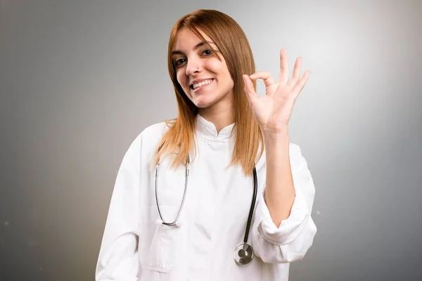 Jonge dokter vrouw Ok aanmelden grijze achtergrond maken — Stockfoto