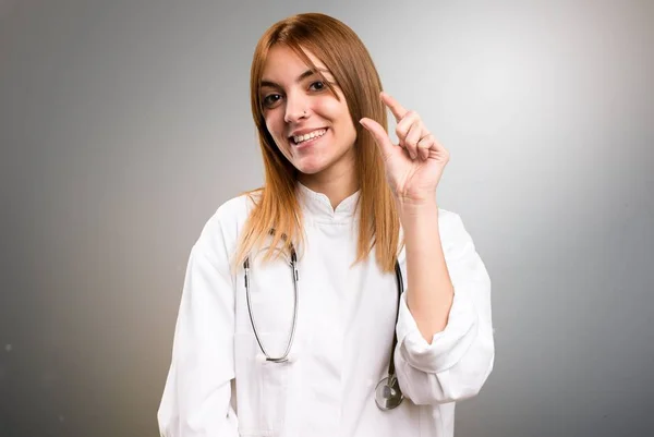 Молодая доктор женщина делает крошечный знак на сером фоне — стоковое фото