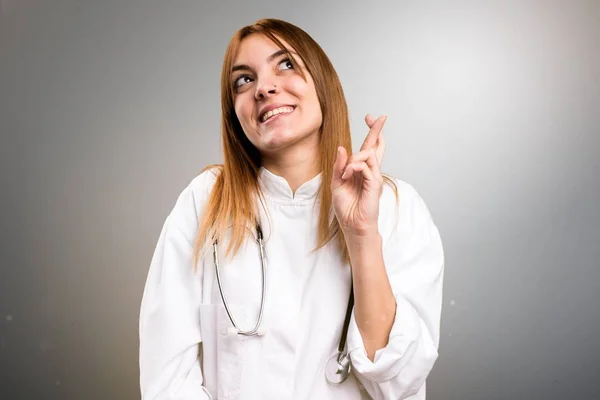 Jeune médecin femme avec les doigts croisés sur fond gris — Photo