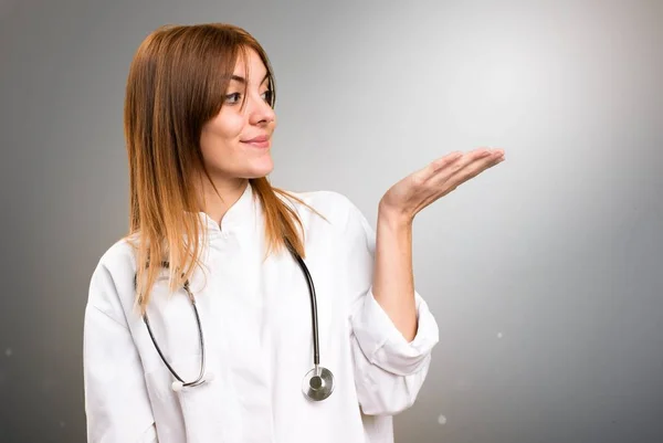 Junge Ärztin hält etwas auf grauem Hintergrund — Stockfoto