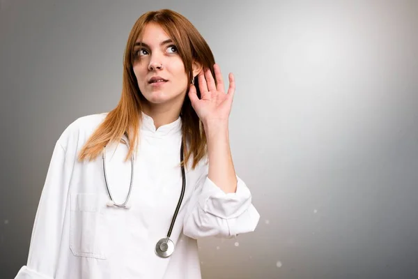 Jonge dokter vrouw luisteren iets op grijze achtergrond — Stockfoto
