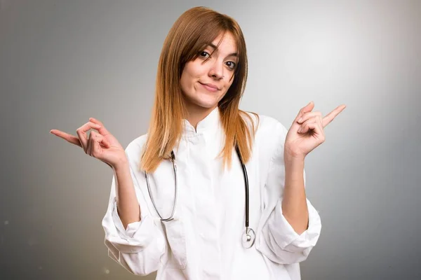 Молода жінка-лікар, яка вказує на латеральні сумніви на сірому фоні — стокове фото