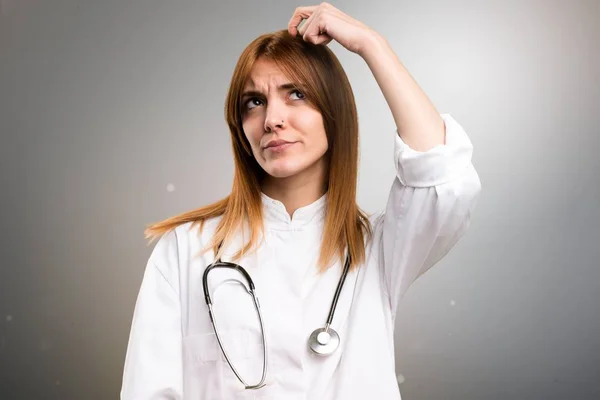 Fiatal doktor nő, kétségek a szürke háttér — Stock Fotó