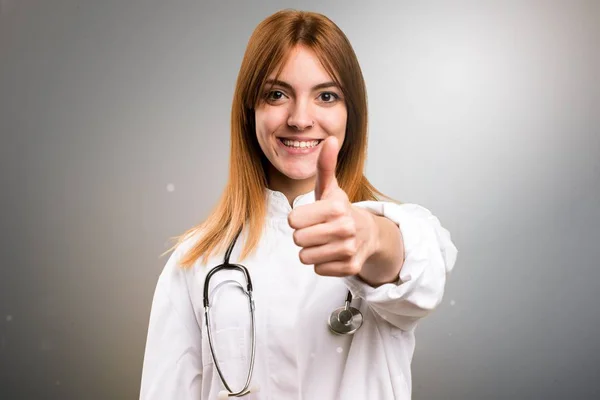 Fiatal orvos nő hüvelykujj a szürke háttér — Stock Fotó