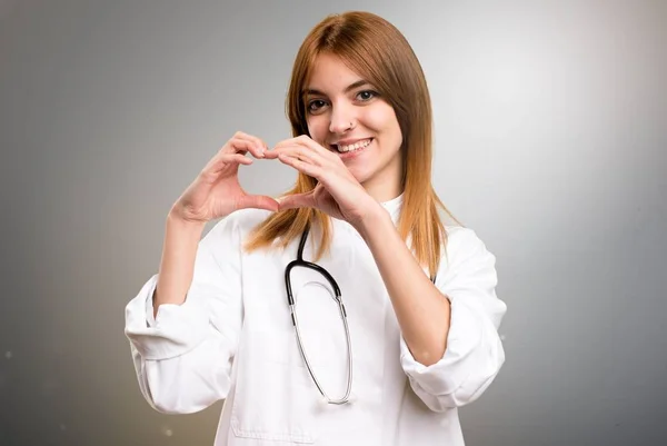 Νέος γιατρός γυναίκα κάνοντας μια καρδιά με τα χέρια σε γκρίζο φόντο — Φωτογραφία Αρχείου
