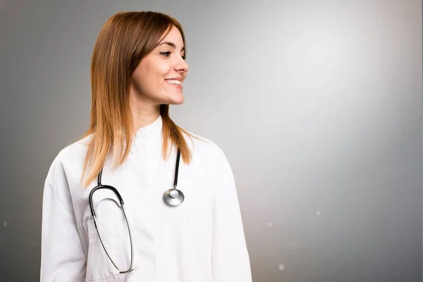 Jovem médico mulher olhando lateral no fundo cinza — Fotografia de Stock