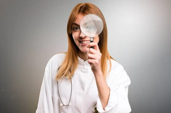 Молодая врач женщина с увеличительным стеклом на сером фоне — стоковое фото