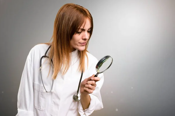 Jonge dokter vrouw met vergrootglas op grijze achtergrond — Stockfoto